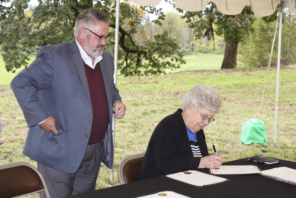 Emma Schmid, matriarch of the Washougal Schmid family, signs a deed to the city for 17.88-acre parcel near the Washougal River that her family has owned since the 1950s. To her left, Washougal Mayor Sean Guard watches the deed signing on Thu., Oct. 6. Photo by Kelly Moyer.
