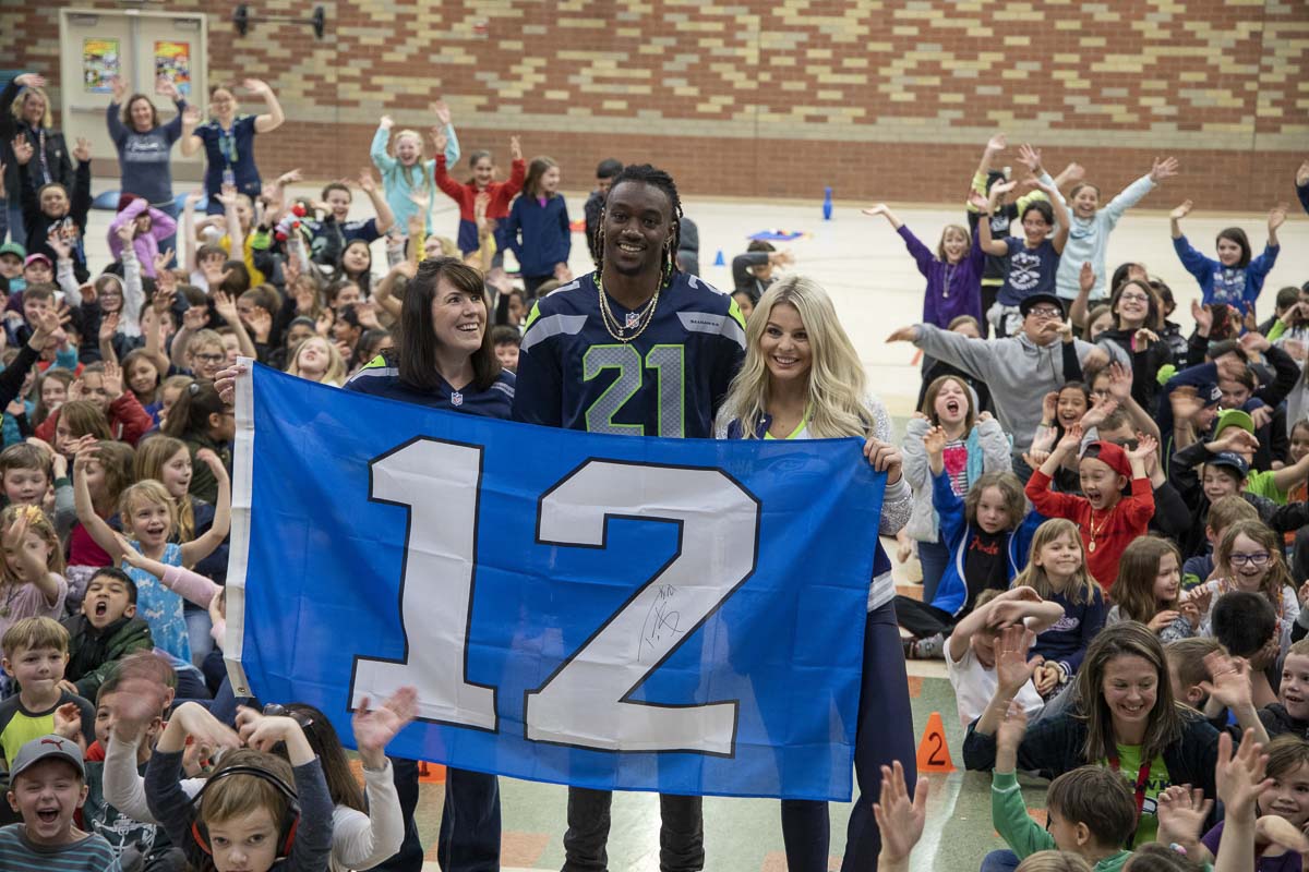Seattle Seahawks cornerback Trey Flowers, Seahawks Dancer Kylie, and York Elementary School Principal Dawn Harris hold a 12th Man flag during assembly on Monday. Photo by Chris Brown