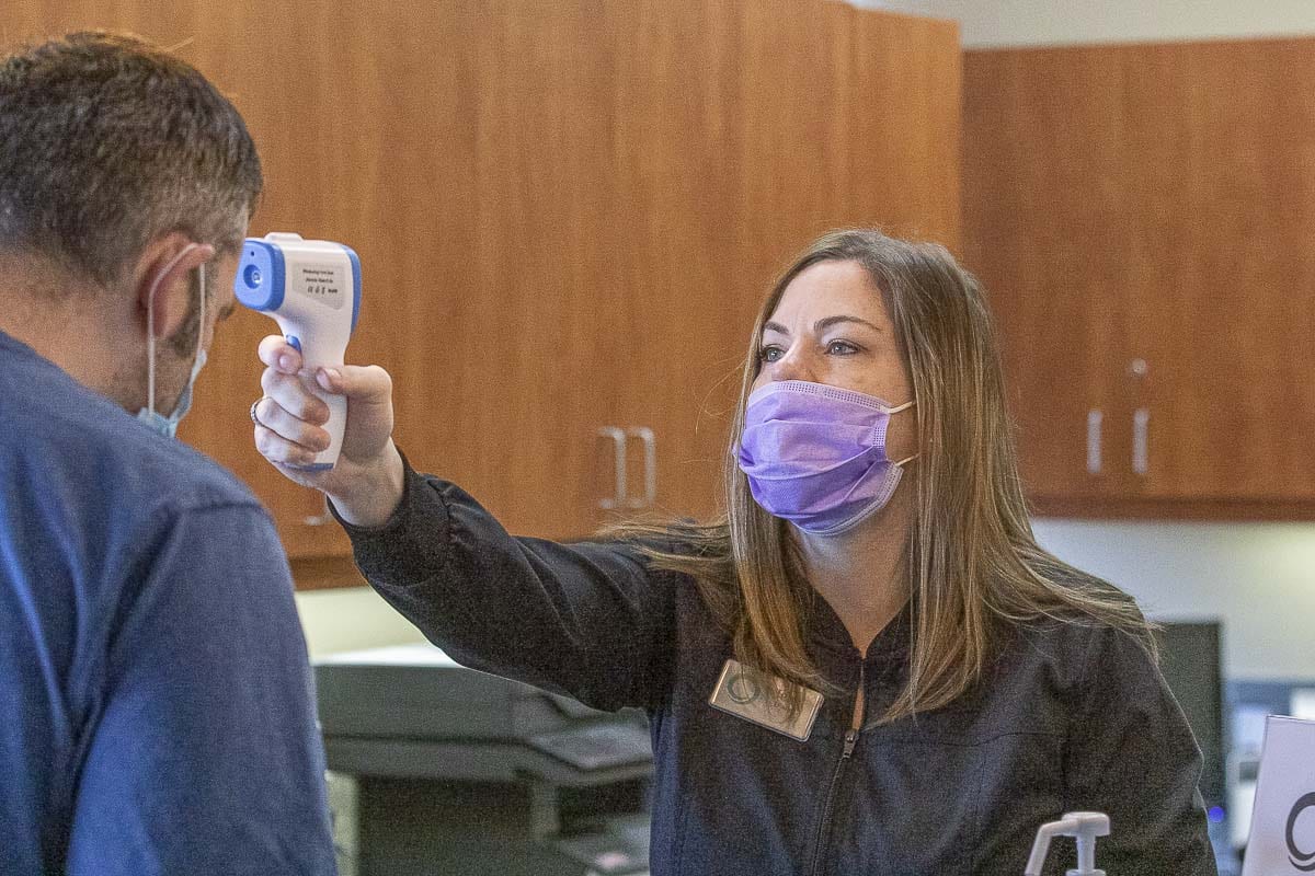 At the Smiles Dental office in Camas, front desk administrator Jena Ewald is seen checking patient Dan Stoica’s temperature prior to his appointment. Photo by Mike Schultz