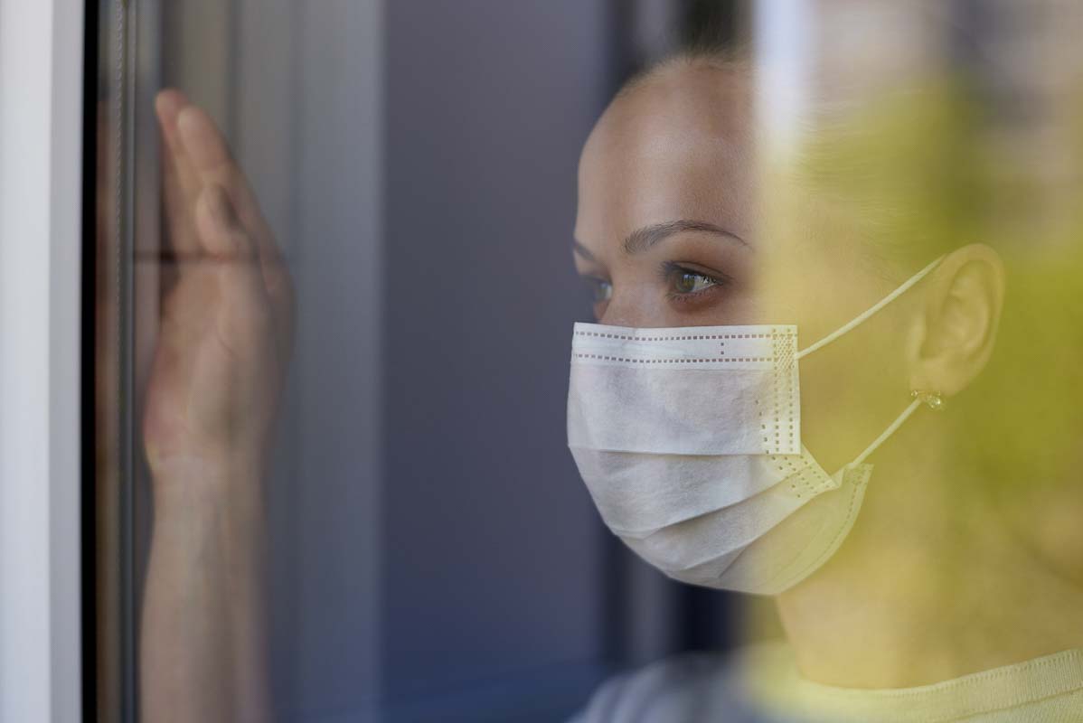 An unidentified woman looks out the window while wearing a mask. Stock Photo