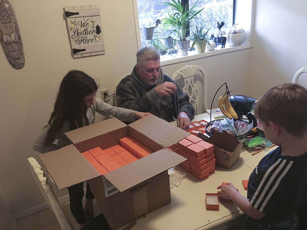 Scott Hampel (center) and his two grandchildren are shown here preparing their necklaces, bracelets and keychains for sale, donation and shipment. Photo courtesy of Scott Hampel