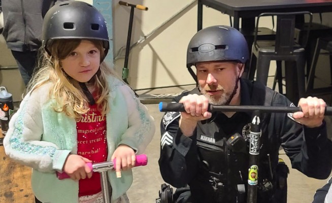 Sgt. Kyle Kinnan of the Washougal Police Department gets tips from 6-year-old Henley on how to ride a scooter on Friday night, part of the Skate with a Cop event at Lunch Money Indoor Skate Park. Photo by Paul Valencia