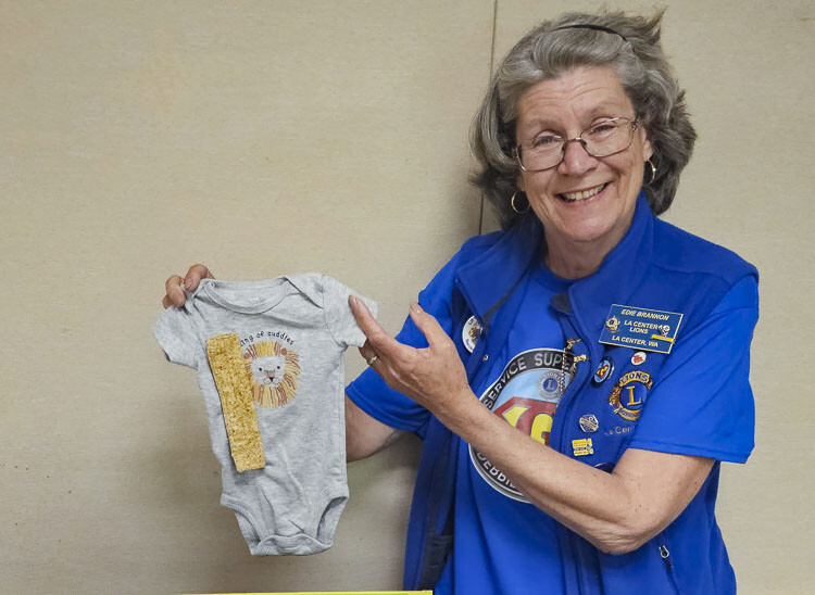 Edie Brannon of the La Center Lions Club holds up one of her Wonderful Onesies, a onesie designed for babies to use while undergoing chemotherapy treatment and other infusions. The La Center Lions Clubs is receiving an international Kindness Matters Award for the Wonderful Onesies Project. Photo by Paul Valencia