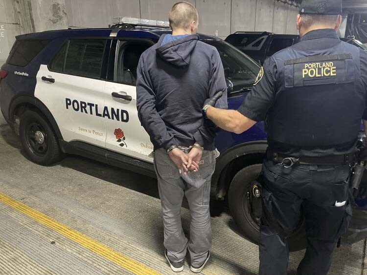 Suspect in Tesla thefts is in handcuffs next to a PPB patrol car, being escorted by an officer. Photo courtesy Portland Police Bureau