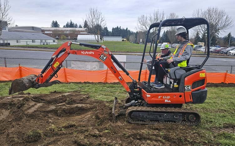 Evergreen student Thomas Cunningham operates an excavator, under the direction of John Jordan of Tapani Inc. Thursday was Dig Day at Evergreen High School, allowing students to get experience with heavy equipment. Photo by Paul Valencia