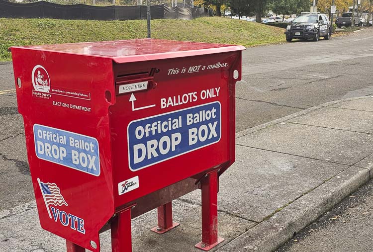 There is a new Official Ballot Drop Box at Fisher’s Landing, and on Tuesday, it was being protected by a Vancouver Police Department officer. Unseen: An observer working for Clark County Elections Office was also there. This was the site of a crime early Monday morning when another drop box was damaged by fire, a fire that destroyed or damaged many ballots. Photo by Paul Valencia