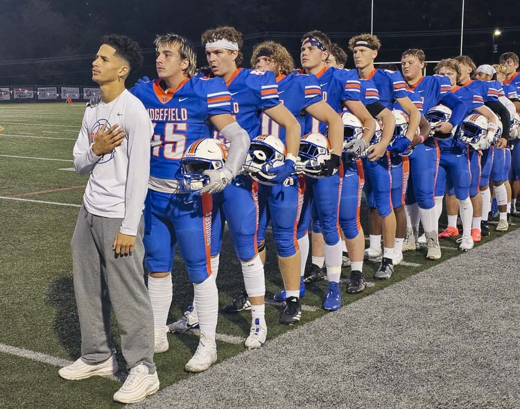 Brian McLemore III stands in front of his Ridgefield football teammates for the national anthem Friday night. McLemore had a life-threatening injury in a freak accident of a play two weeks ago. He will not play the rest of the season, but he remains a big part of the team. Photo by Paul Valencia