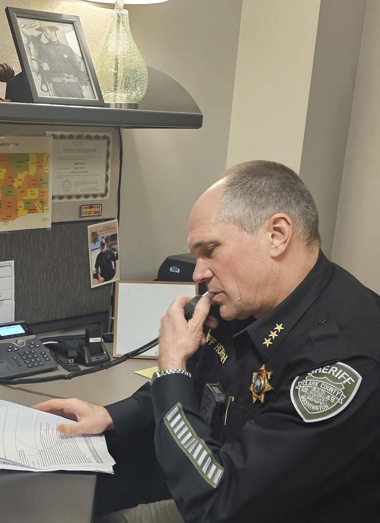 Clark County Sheriff John Horch works the phone at his desk, under the watchful eye of an autographed picture of Clint Eastwood, Horch’s favorite actor. Photo by Paul Valencia